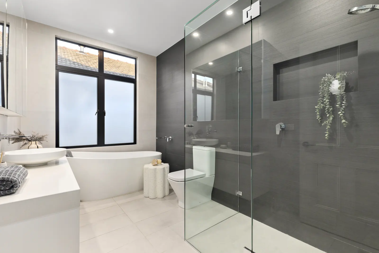 Finished bathroom with freestanding bath, dark tiled wall and frameless shower screen