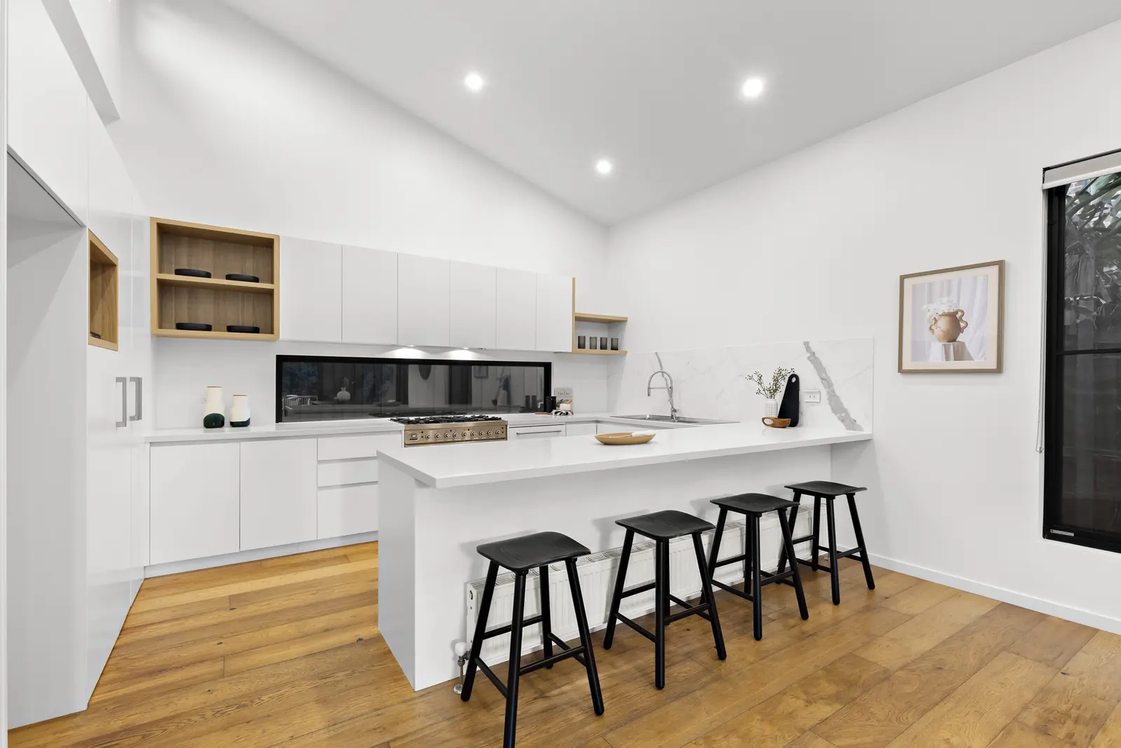 Finished kitchen under the raked ceiling, with a long bench, window splashback, oak shelving and timber floors