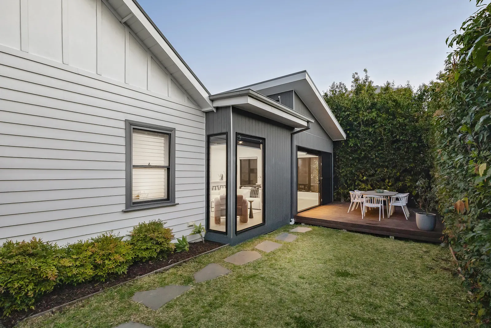 Rear extension in dark vertical cladding meeting the original weatherboard house, with corner glazing and a timber deck